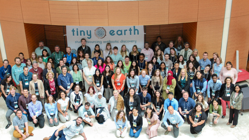 A large group of people who attended a symposium in front of the Tiny Earth banner.