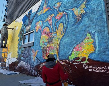 Two people working on painting a mural on the side of a wall.