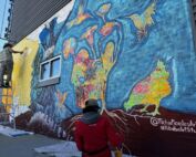 Two people working on painting a mural on the side of a wall.