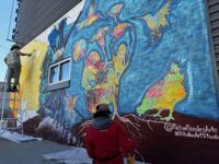 Two people working on painting a mural on the side of a wall.