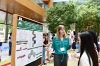 A woman is talking about a scientific poster in front of two students.