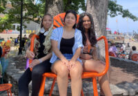 Three students sit on an oversized chair.
