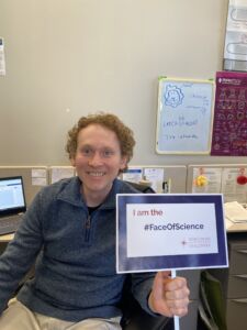 Ross Schwartz sitting in his cubicle participating in the I am the face of science event
