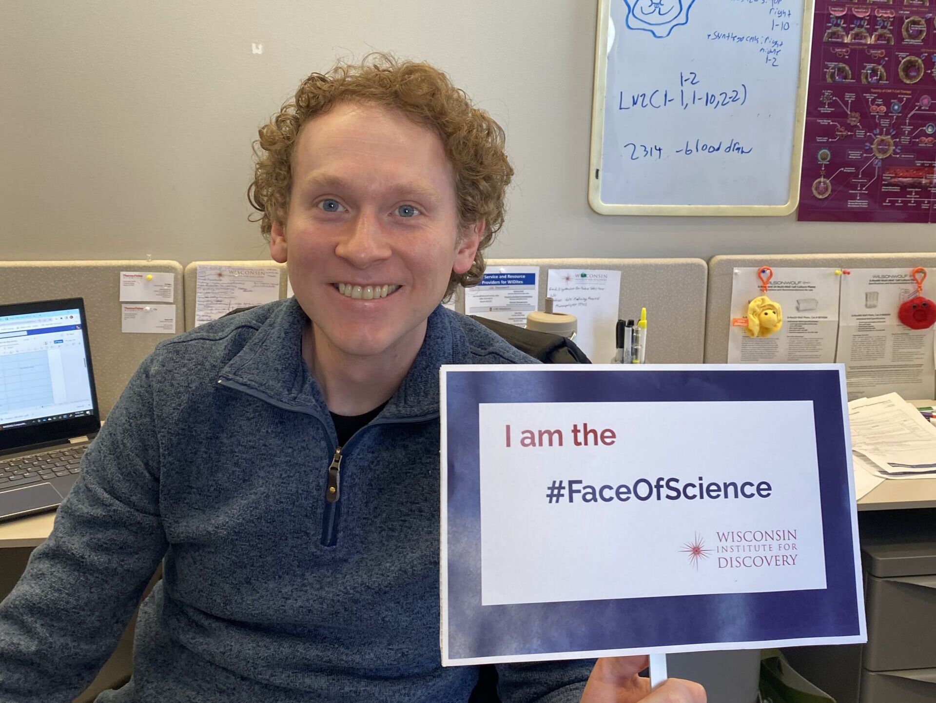 Ross Schwartz sitting in his cubicle participating in the I am the face of science event