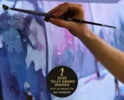 A hand holds a paint brush and is making a stroke on canvas.