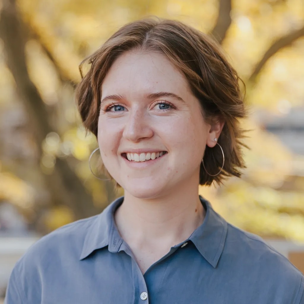 A woman with short hair wearing a blue collared shirt smiles.