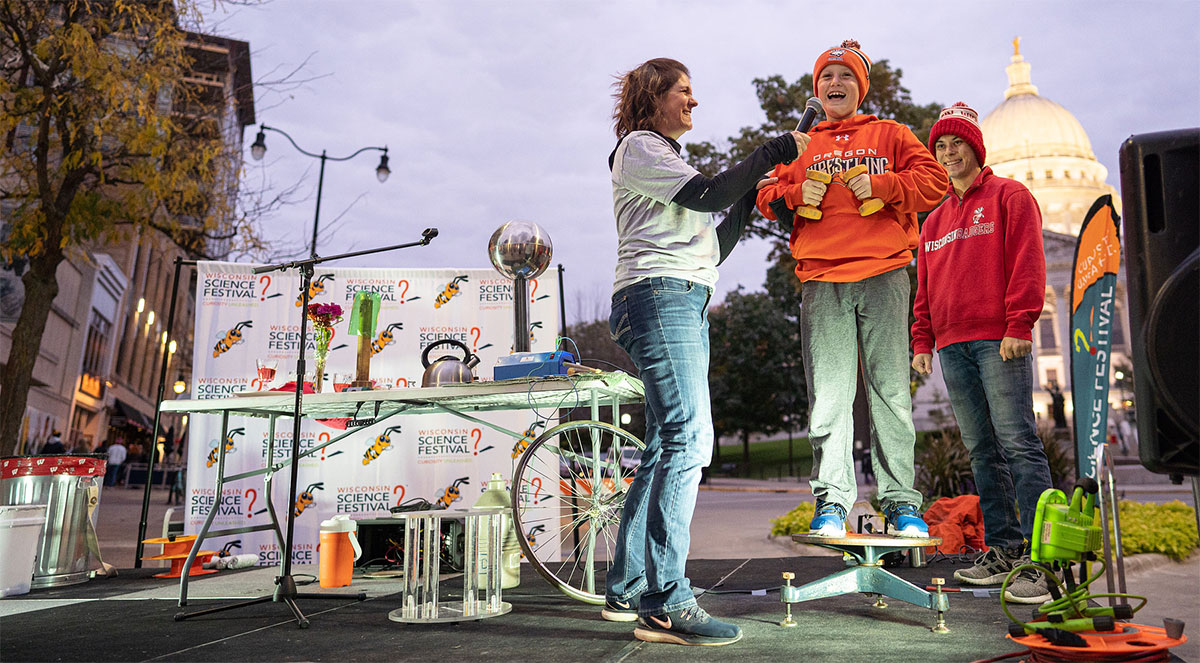 Scientists stand on a podium outside wearing casual clothes at dusk